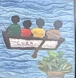 Quilted panel showing four children seated in a small wooden boat labeled 'Cora' on rippling blue water, with a green plant in the foreground